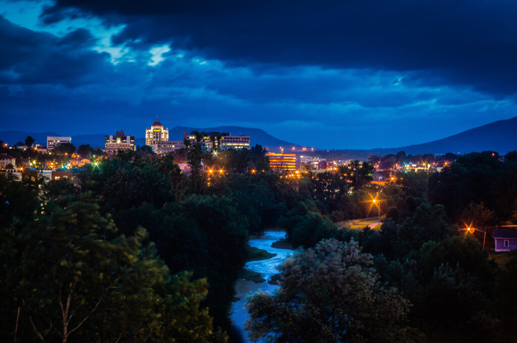 shot of the Roanoke skyline lit up at dusk with the Roanoke River in the foreground.