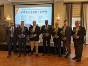 Several men holding plants smiling at the camera in a conference room