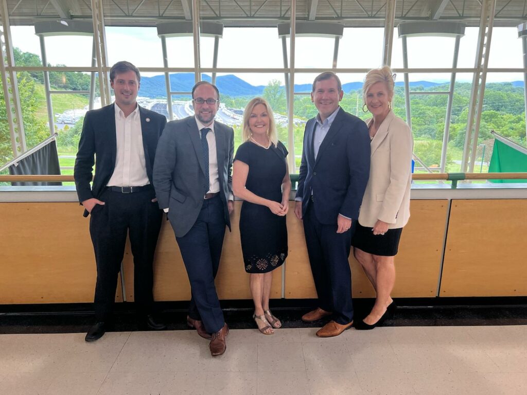 Five people smiling and posed in front of large window with mountains in the background