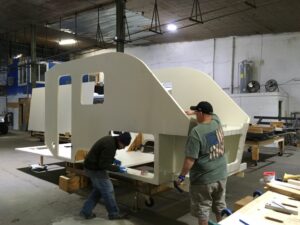 Two men in a warehouse putting together the frame of a small camper trailer