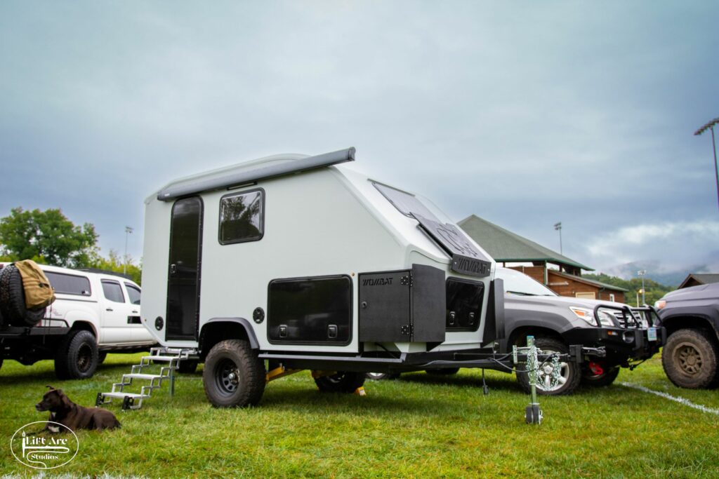 overland-style, small camper parked in the grass with a dog laying in front of it