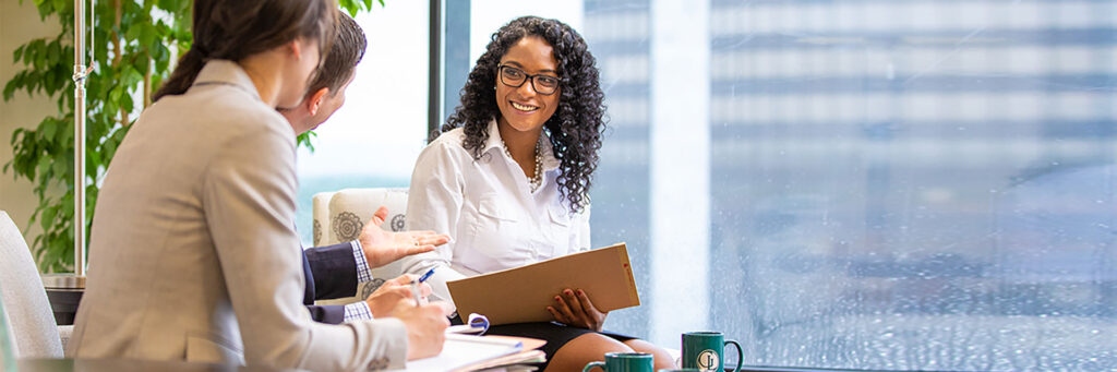 Young black woman working in a downtown office building smiles while talking with two colleagues