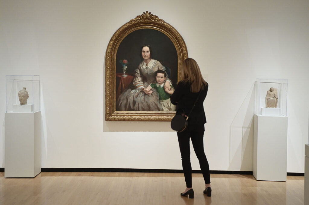 A woman from behind as she looks on at a painting in an art museum.
