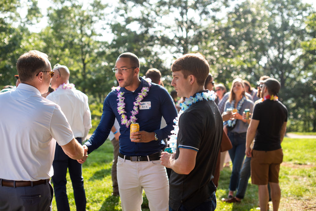 Young Black man shakes hands with middle-aged white man at an outdoor social event.