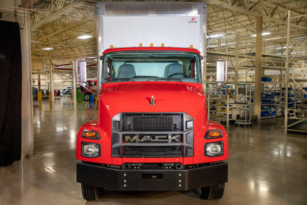 Red Mack Truck with white trailer parked inside of a warehouse.