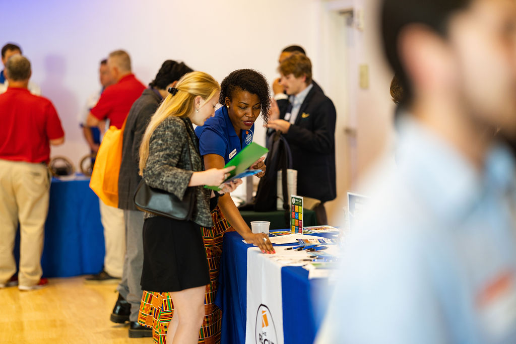 An African-American woman at a job fair explains employment opportunities to a young white woman.