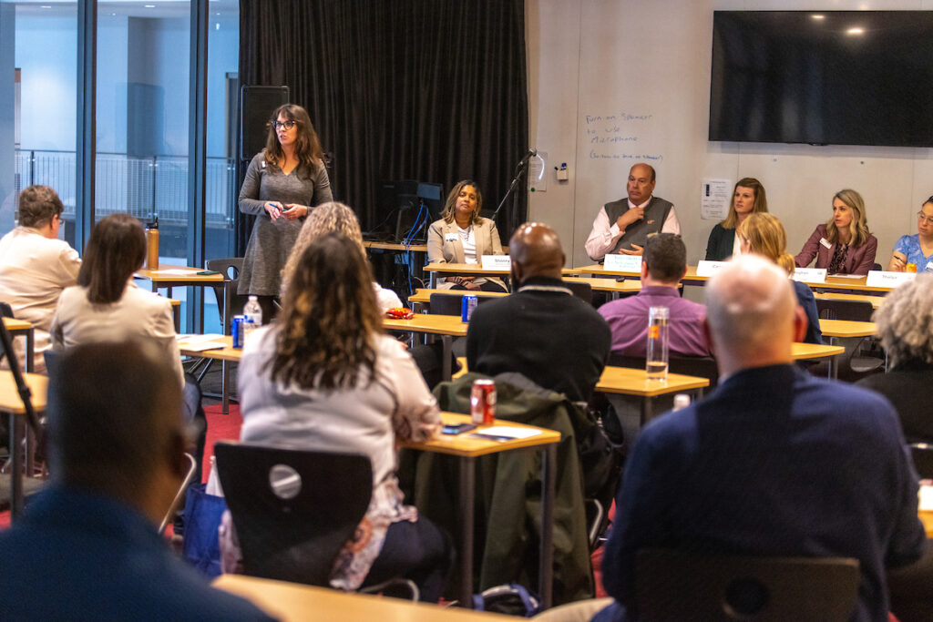 People seated in a classroom as they listen to a panel discussion.