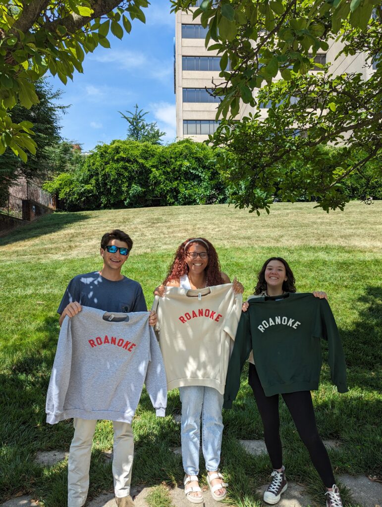 Group of young professionals holding Roanoke sweatshirts outside