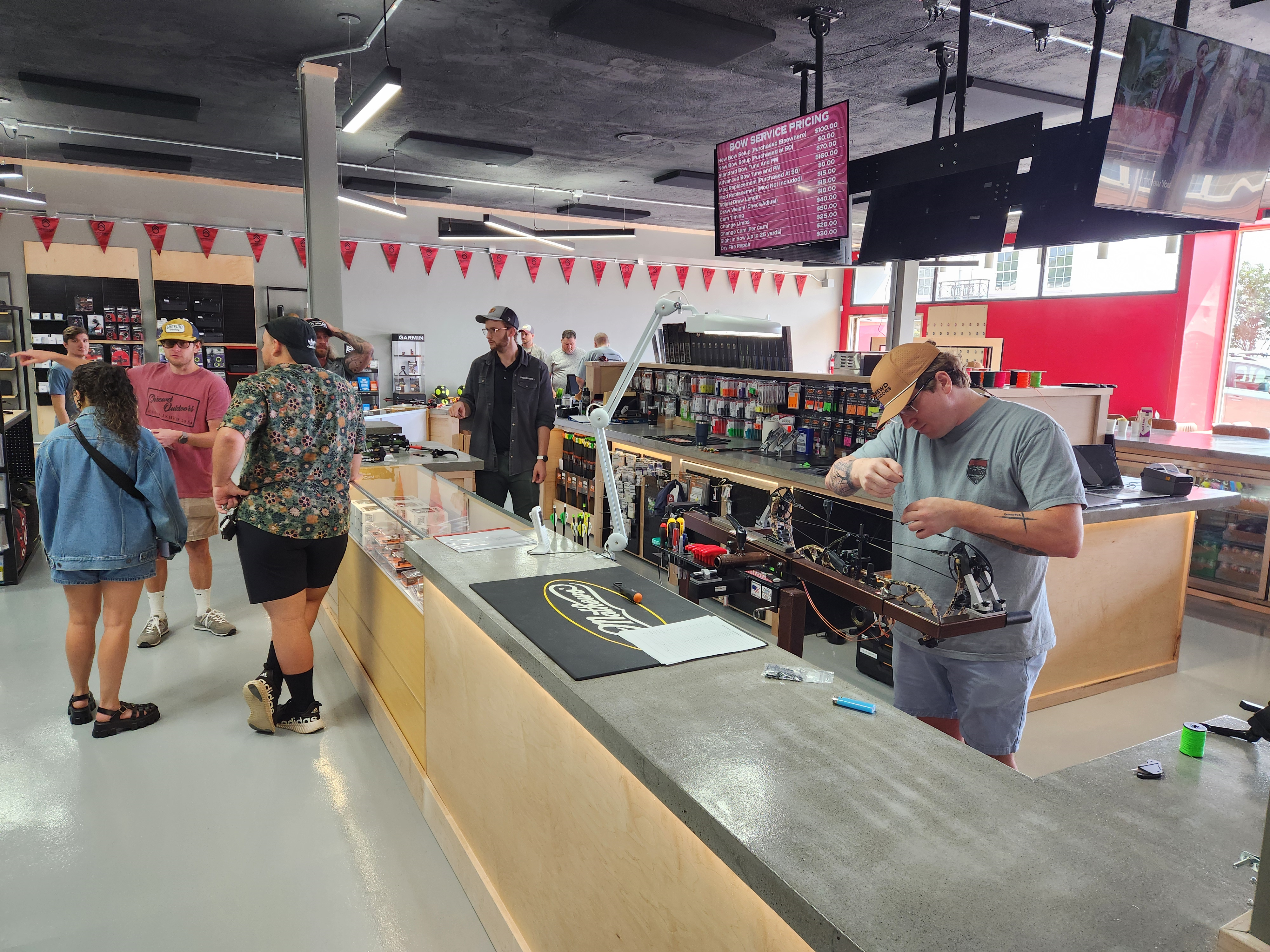 Shrewd Outdoors Grand Opening in Salem, VA. People gather around a counter while someone works on an archery bow.