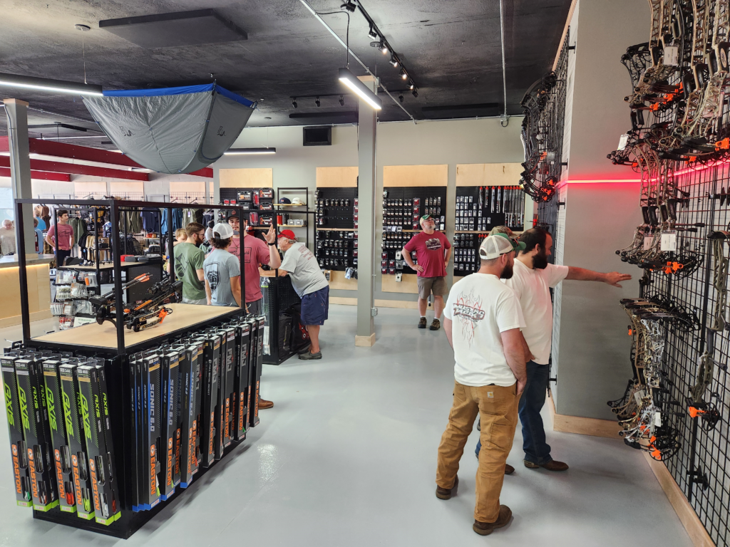 Interior of Shrewd Outdoors in Salem, VA. There are people milling about in a brightly lit, open store with archery equipment stocking displays.