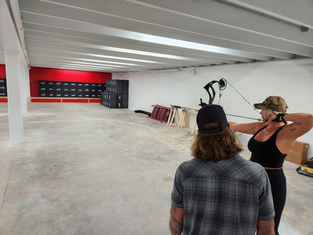 The back of a man's head as he instructs a young woman who is practicing archery at Shrewd Outdoors in Salem, VA.