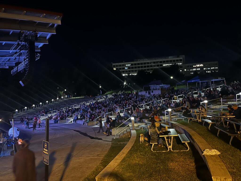 A crowd of people sit in an outdoor amphitheater, Elmwood Park, at night as they watch the MountainFilm Festival at Roanoke GO Outside Festival