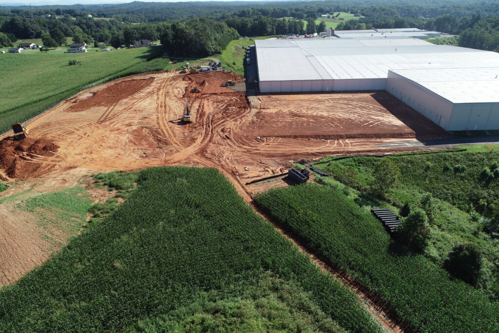 A large shell building with excavation and grading work taking place behind it. There is construction equipment on the construction pad on a sunny day.