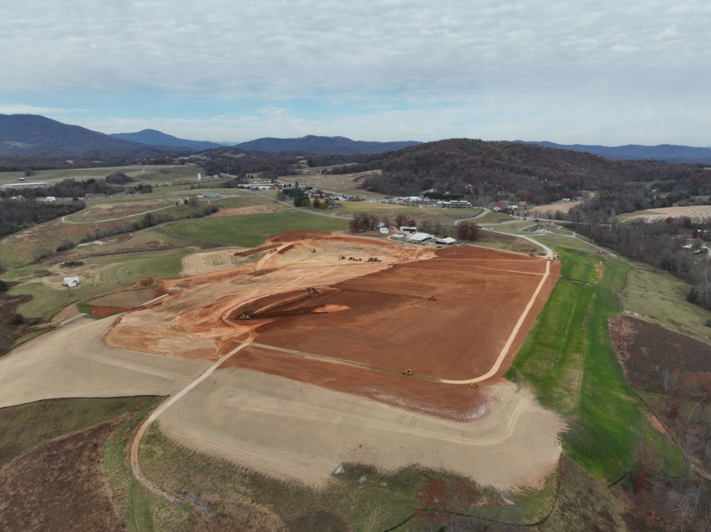 A site being graded for the construction of a building. There is construction equipment on the site and mountains in the background. 